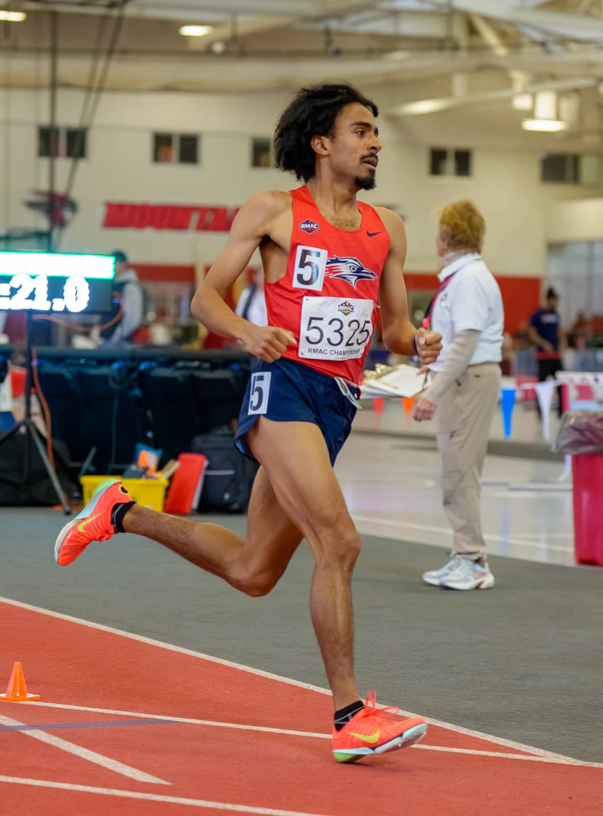 Darren Hayden running on an indoor track in his red collegiate racing uniform.